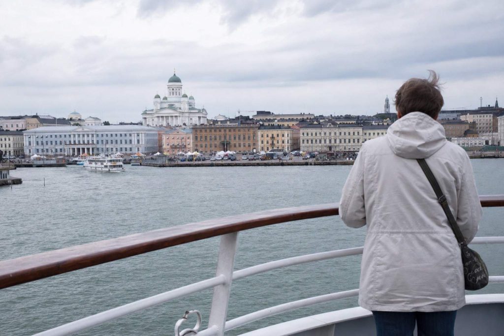 A traveller at a ferry railing looking toward Helsinki's harbour skyline