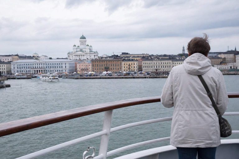 A traveller at a ferry railing looking toward Helsinki's harbour skyline