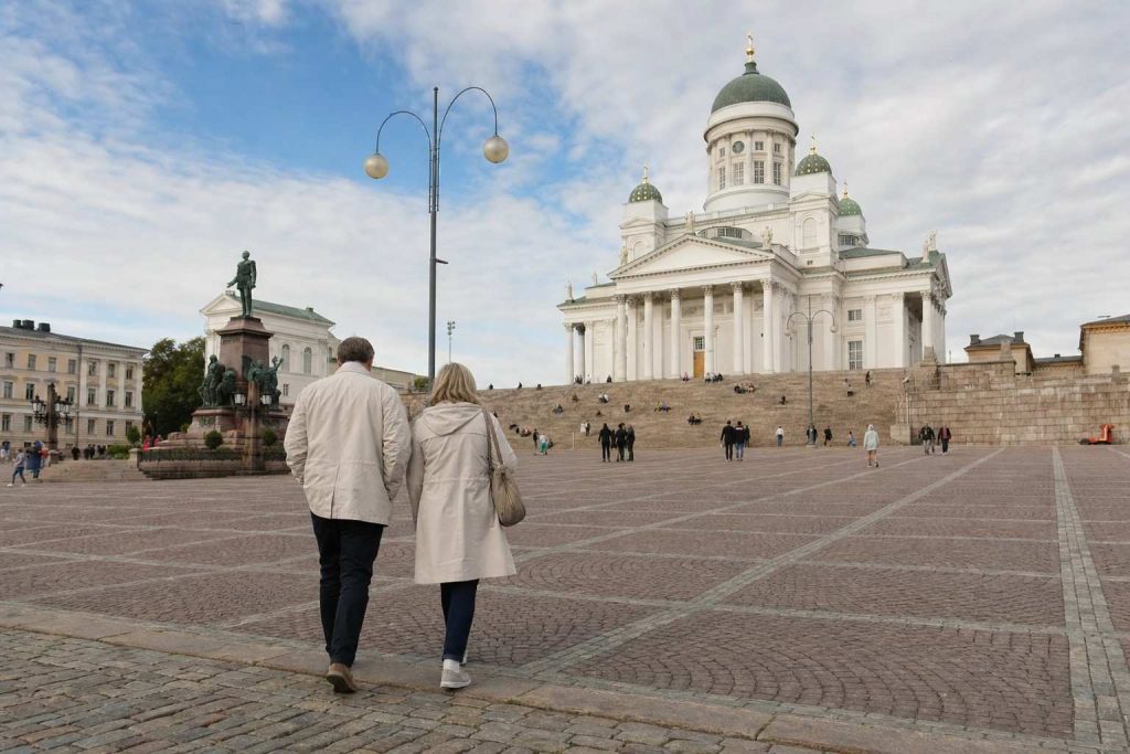 A couple walking across Senate Square toward Helsinki Cathedral in soft daylight