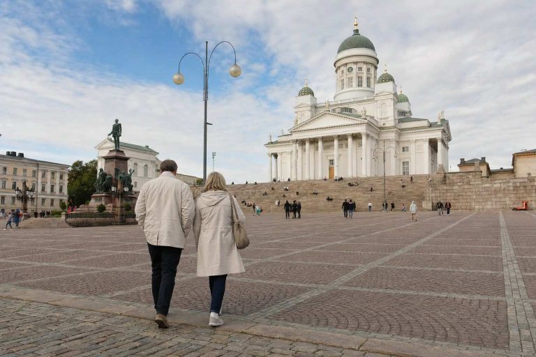 A couple walking across Senate Square toward Helsinki Cathedral in soft daylight